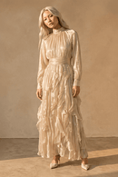 Woman wearing a long, flowing beige dress against a neutral background