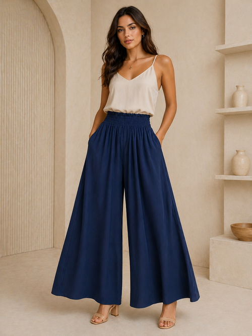 Woman wearing a white top and blue wide-leg pants in a neutral setting