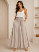 Woman wearing a white top and beige wide-leg pants in a minimalistic room.