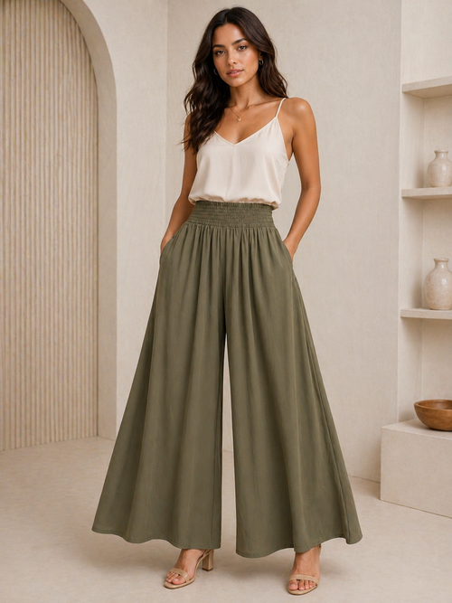 Woman wearing a white top and olive green wide-leg pants in a neutral setting.