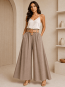 Woman wearing a white top and beige wide-leg pants in a neutral setting