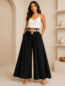 Woman wearing a white top and black wide-leg pants with a beige belt, standing in a neutral-colored room.